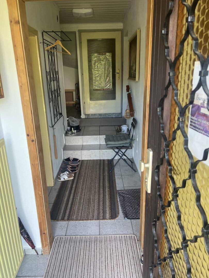 Eingangsbereich mit Treppe, Fliesenboden und einer Garderobe in einem älteren Gebäude.