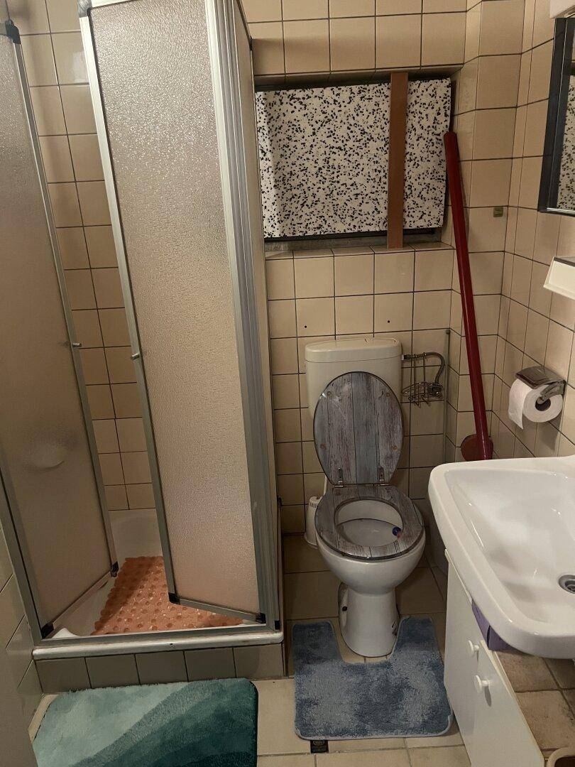 Badezimmer mit Dusche, WC und Waschbecken, ausgestattet mit hellen Fliesen im Stil der 80er Jahre.