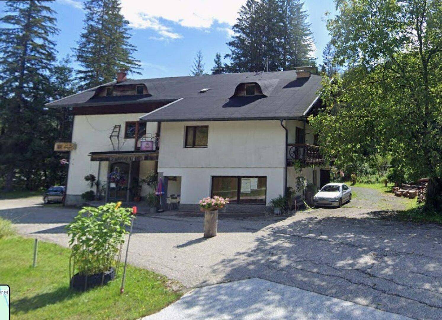 Traditionelles Gebäude mit dunklem Dach und Balkonen, umgeben von grüner Natur.