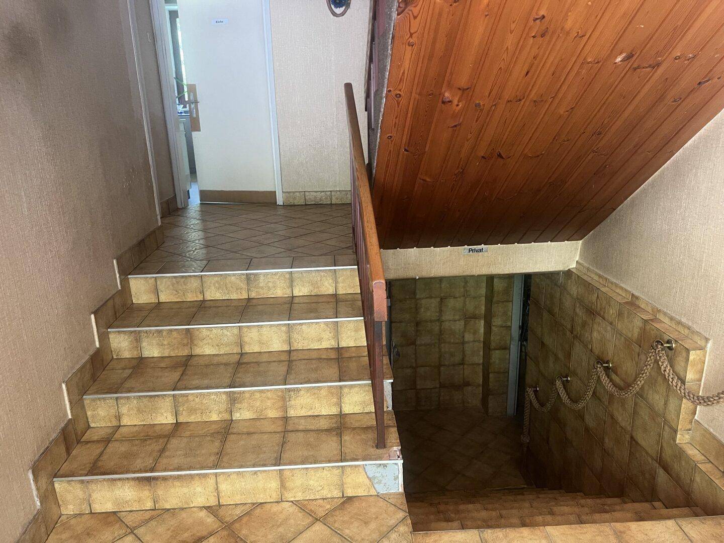 Treppenhaus mit gefliesten Stufen und Holzgeländer, führt in den Kellerbereich.