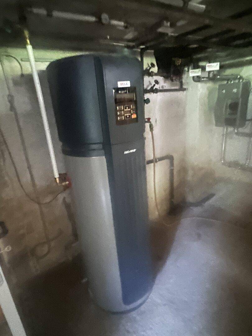 Heizungsraum mit modernem Warmwasserspeicher und sichtbaren Rohrleitungen.