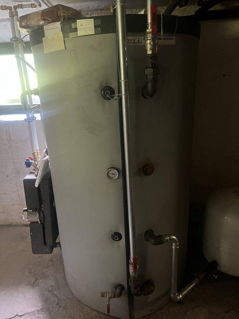 Großer Warmwasserspeicher im Kellerraum mit sichtbaren Anschlüssen und Leitungen.