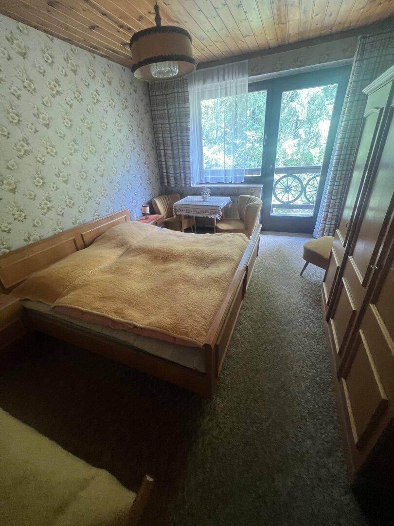 Schlafzimmer mit Doppelbett, floraler Tapete und Zugang zu einem kleinen Balkon.