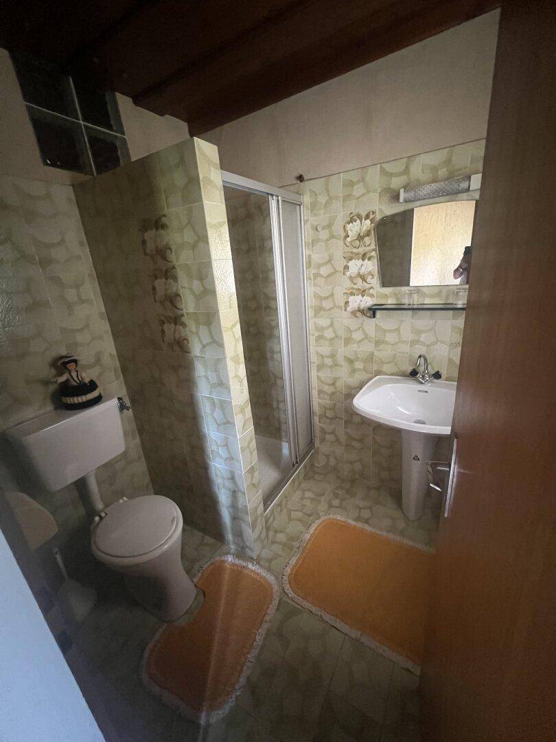Badezimmer mit Duschkabine, WC und Waschbecken, gefliest in hellgrünen Tönen.