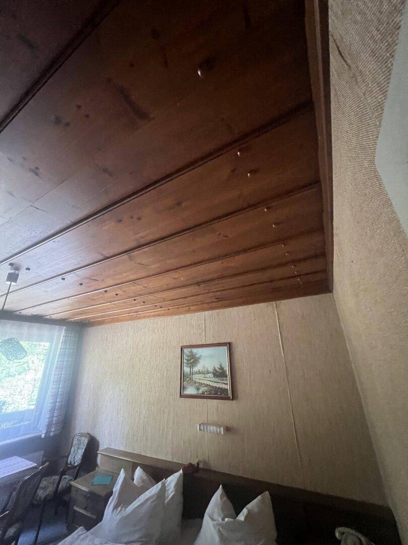 Schlafzimmer mit Holzdachschräge, einfacher Einrichtung und Blick ins Grüne.