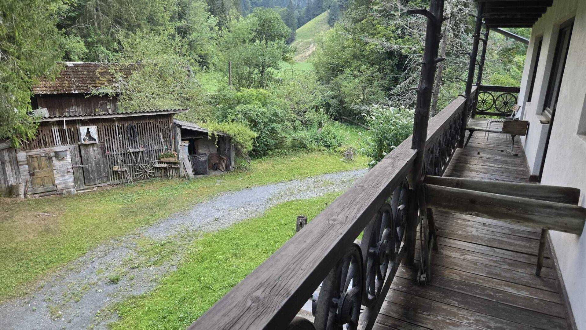 Rustikaler Holzbalkon mit traditionellem Geländer und Blick auf einen alten Schuppen und die grüne Landschaft.