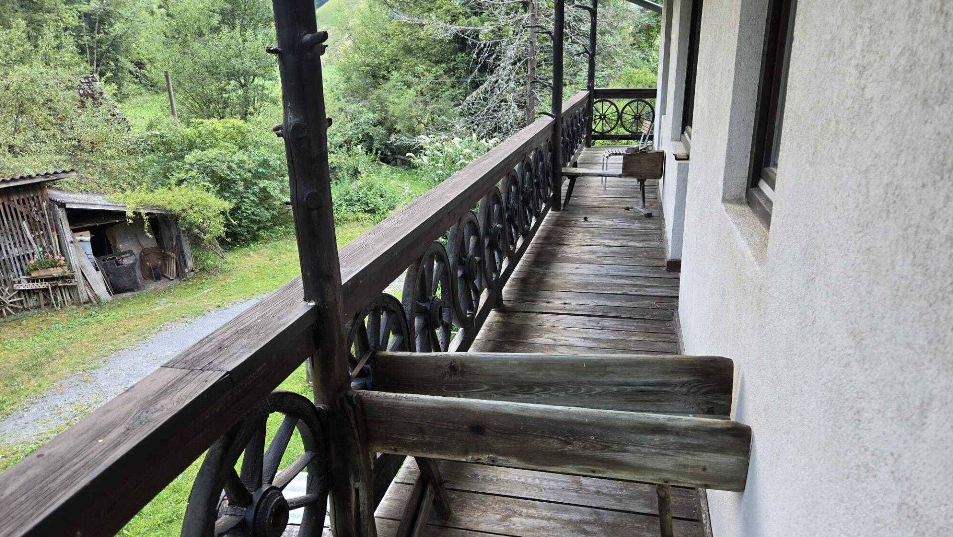 Langer Holzbalkon mit traditionellen Wagenrad-Geländern und weitem Blick in die bewaldete Umgebung.