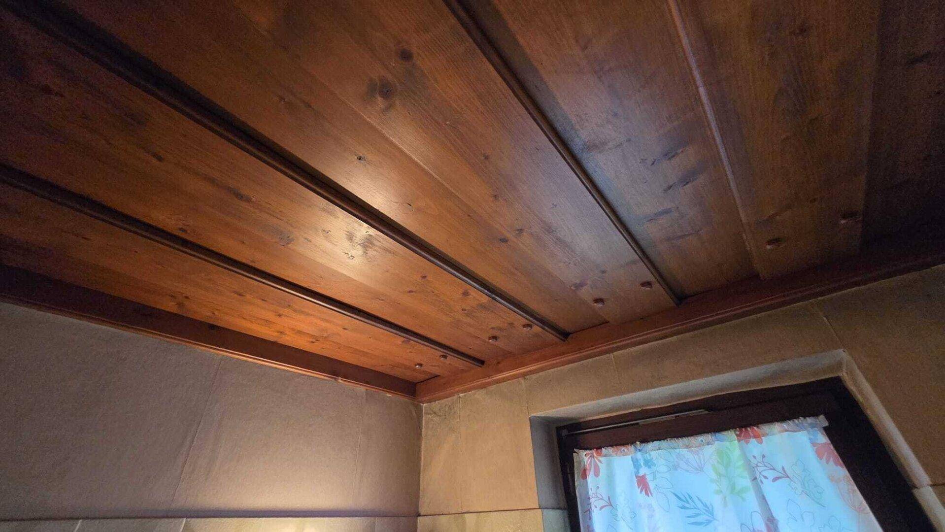 Detailaufnahme einer Holzpaneeldecke und eines Fensters mit gemustertem Vorhang.