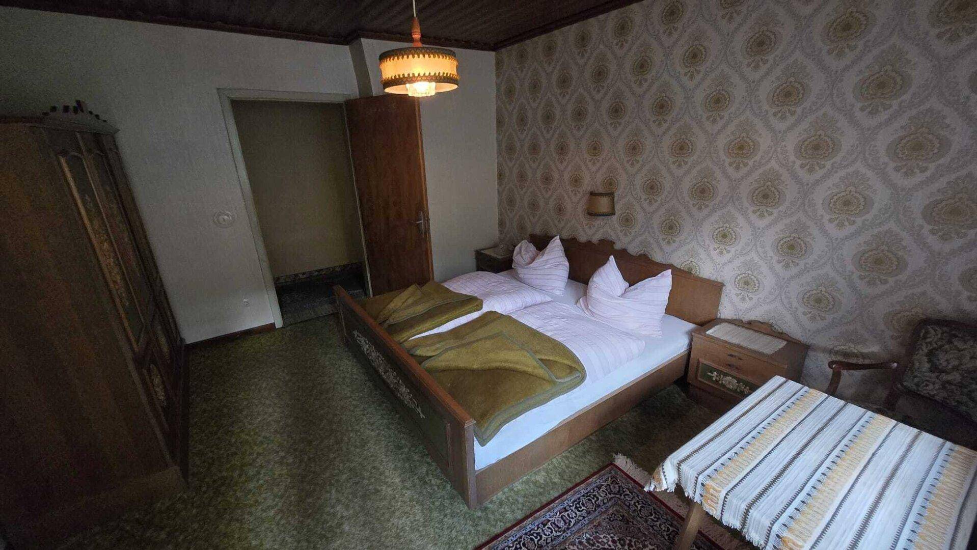 Schlafzimmer mit Doppelbett, Kleiderschrank und gemusterten Tapeten in traditionellem Stil.