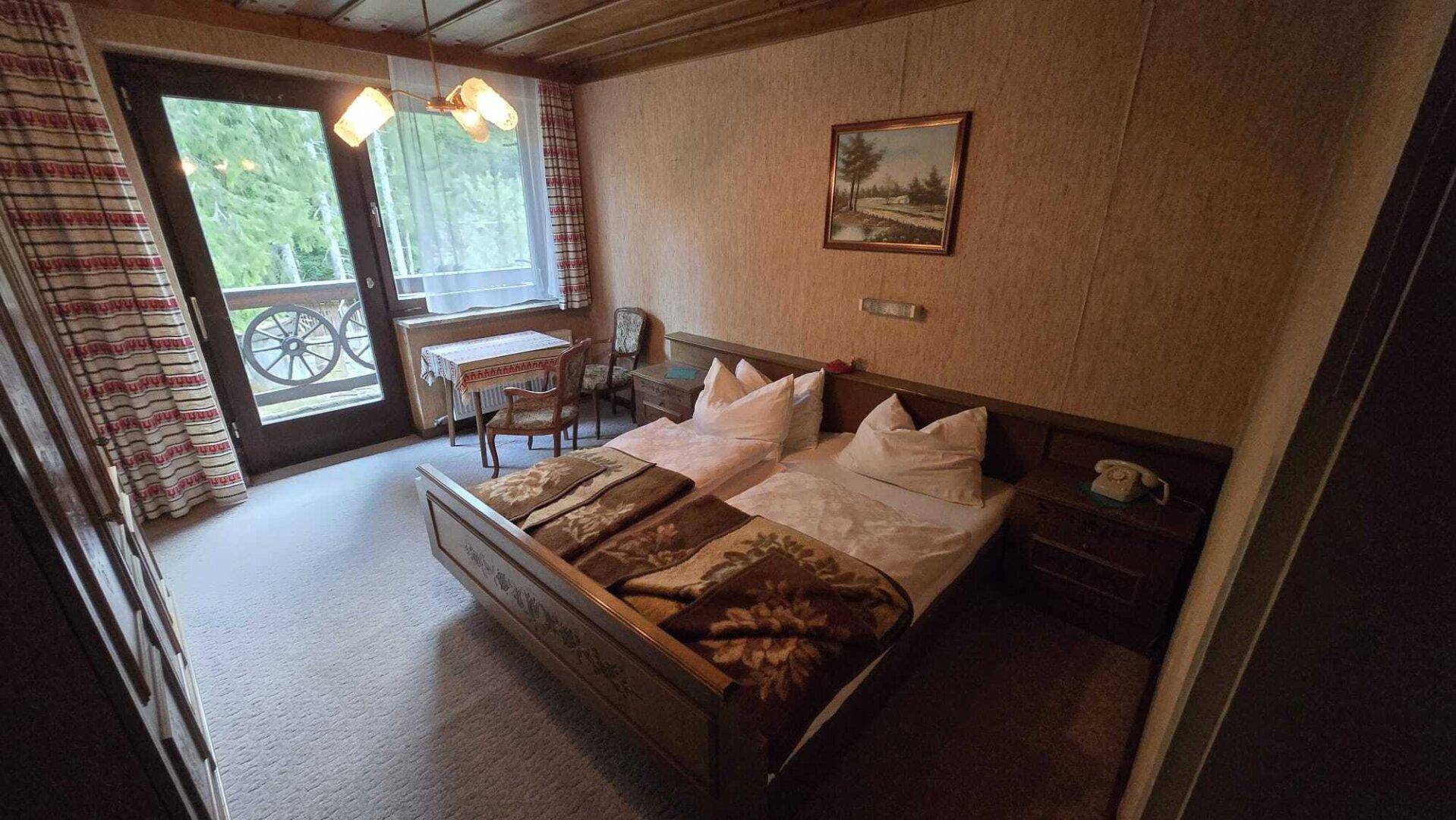 Schlafzimmer mit Zugang zum Balkon, Doppelbett und traditioneller Einrichtung mit Teppichboden.