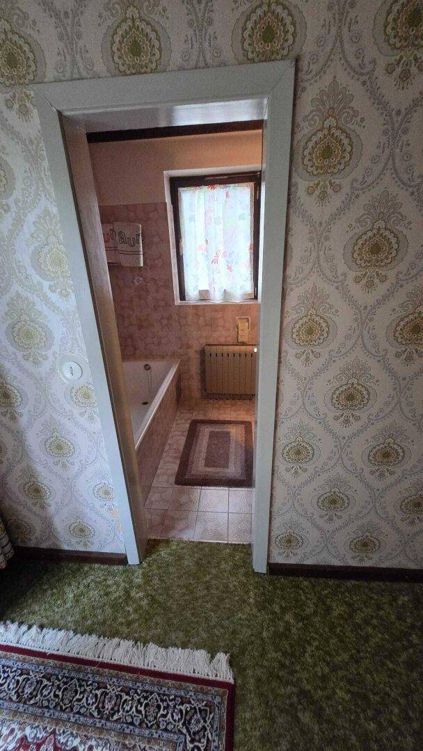 Blick durch eine Tür in ein Badezimmer mit Badewanne, Fliesenboden und Fenster.