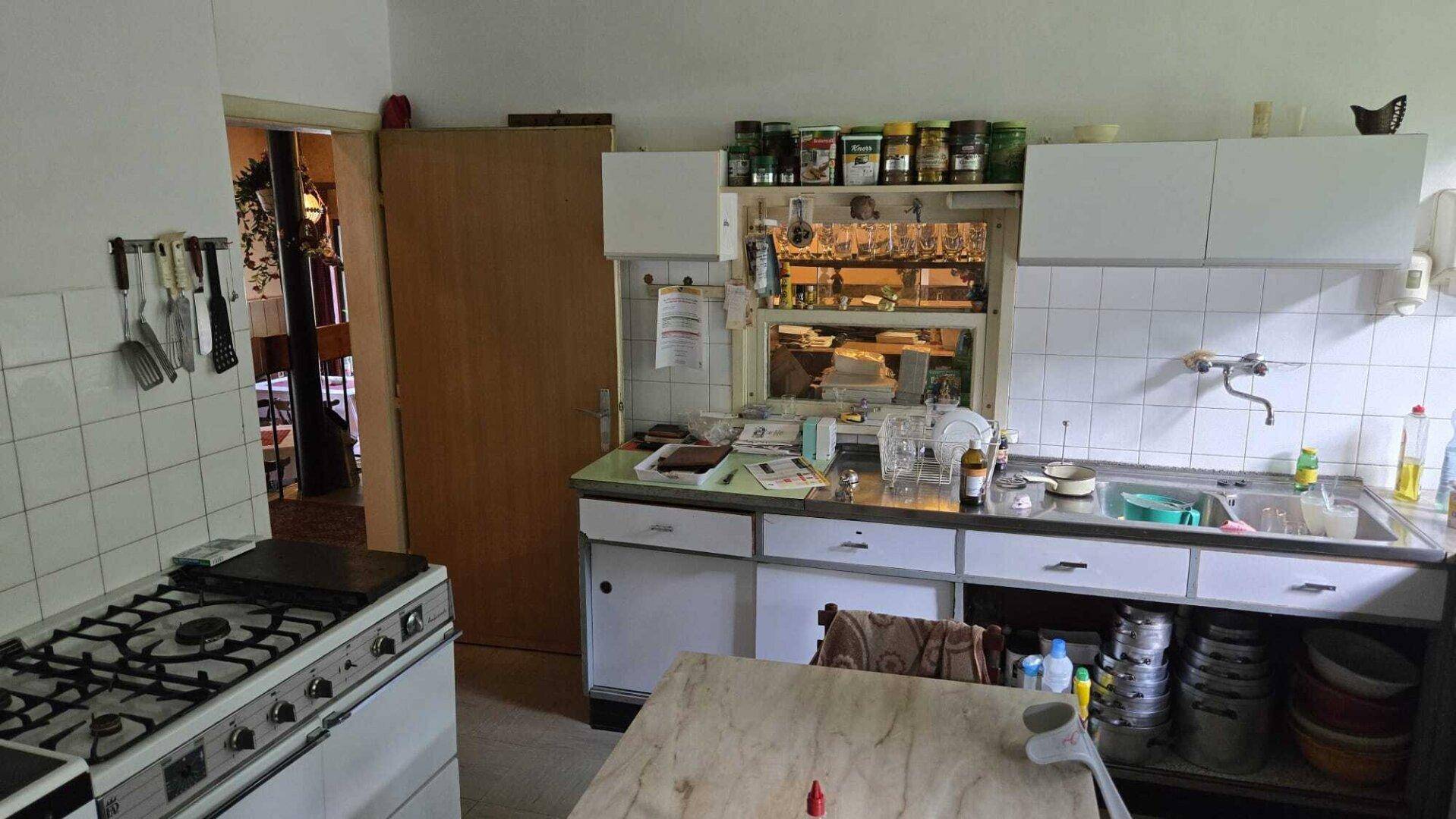 Ältere Küche mit weißen Schränken, Spüle und Gasherd, funktional und traditionell eingerichtet.