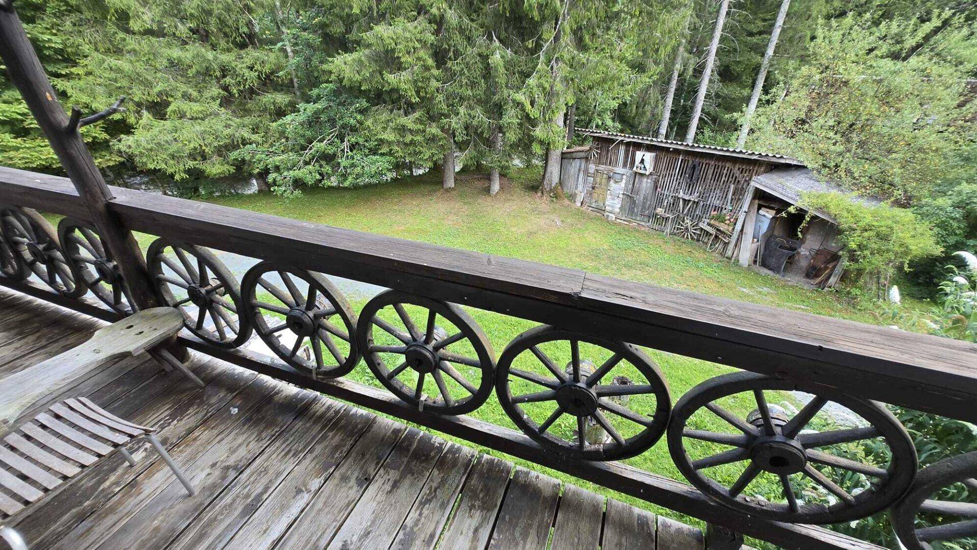 Blick vom Balkon mit rustikalem Holzgeländer und grüner Waldlandschaft im Hintergrund.