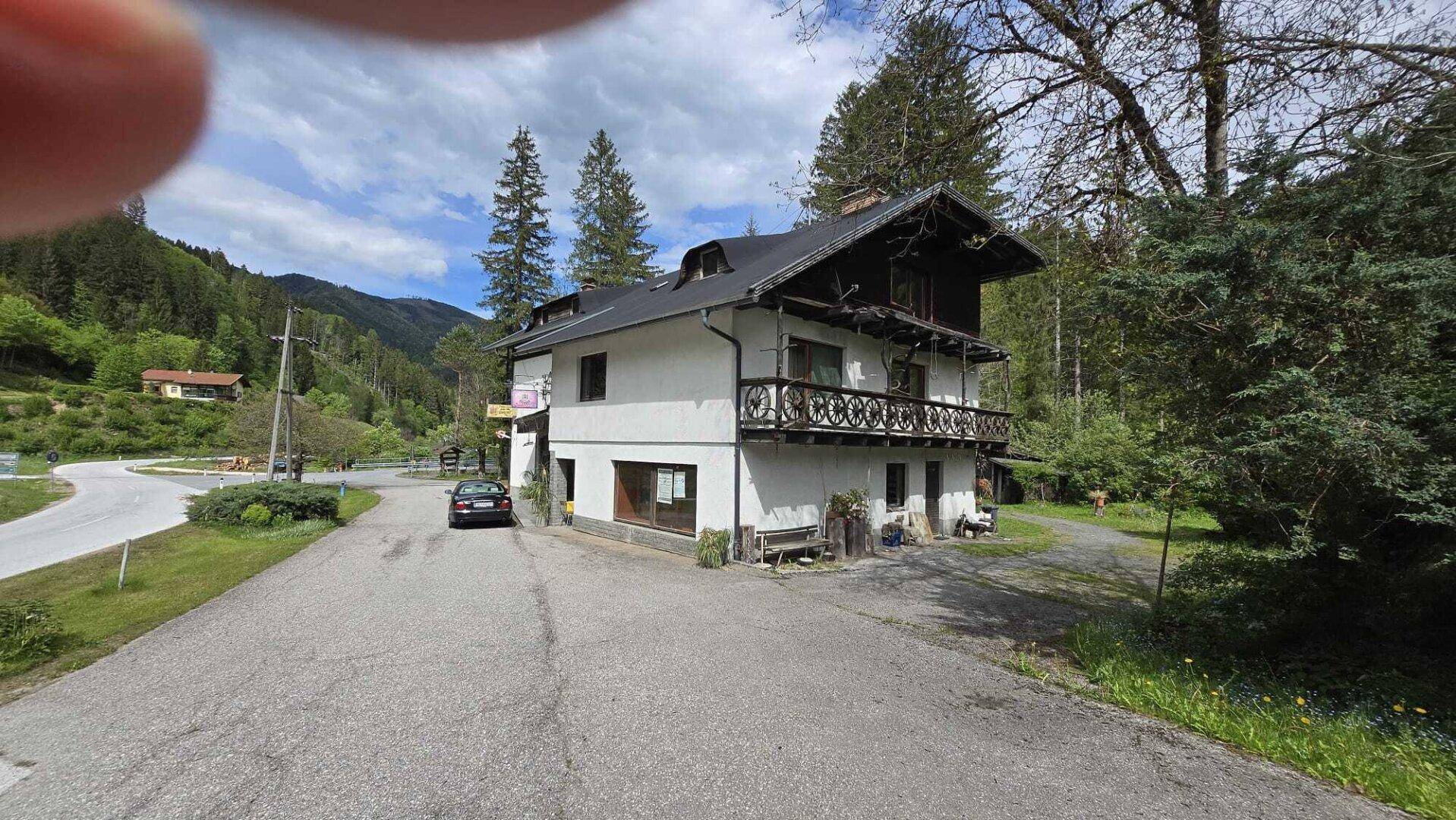 Ansicht des Gebäudes von der Straße mit Eingangsbereich und geparktem Auto vor Bergkulisse.