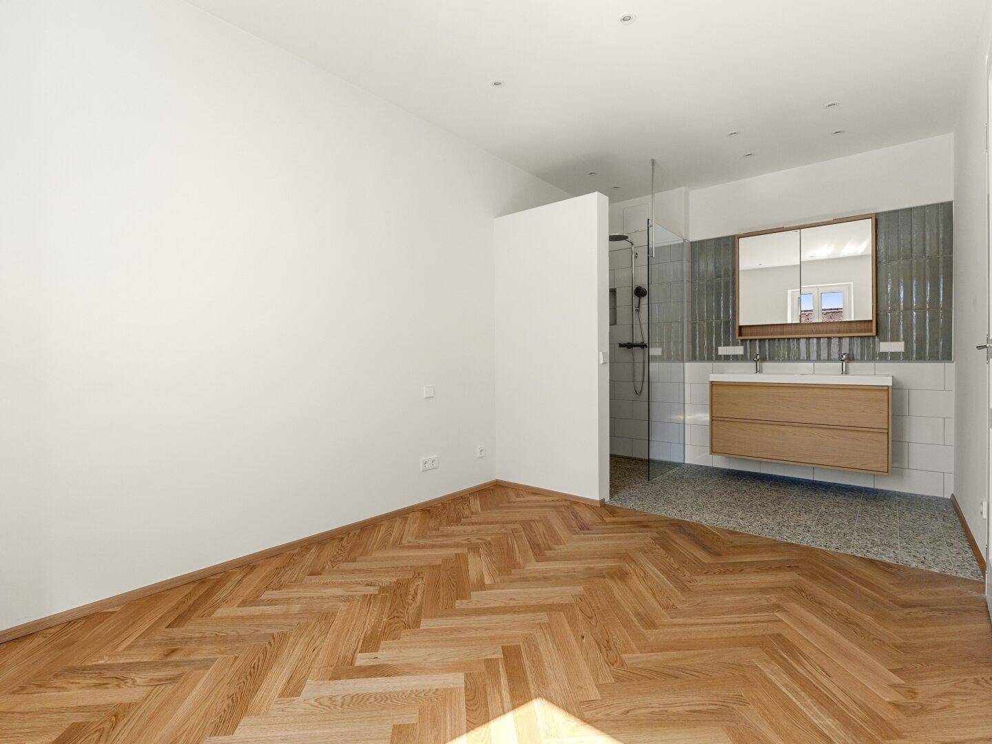 Schlafzimmer mit Fischgrätparkett und offenem Zugang zu einem modernen Duschbereich.