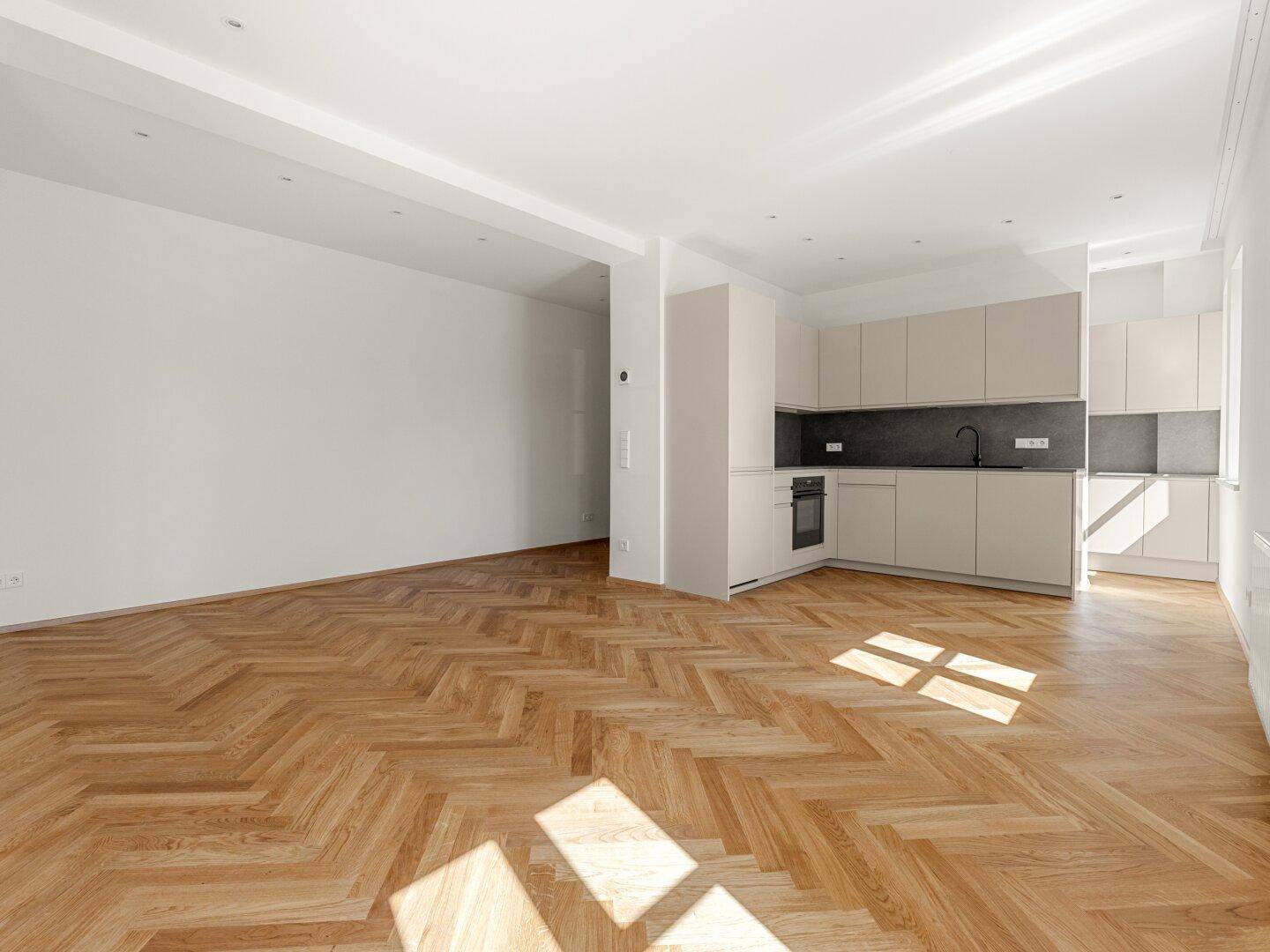Moderne Einbauküche mit hellen Schränken, dunkler Arbeitsplatte und Fischgrätparkettboden.