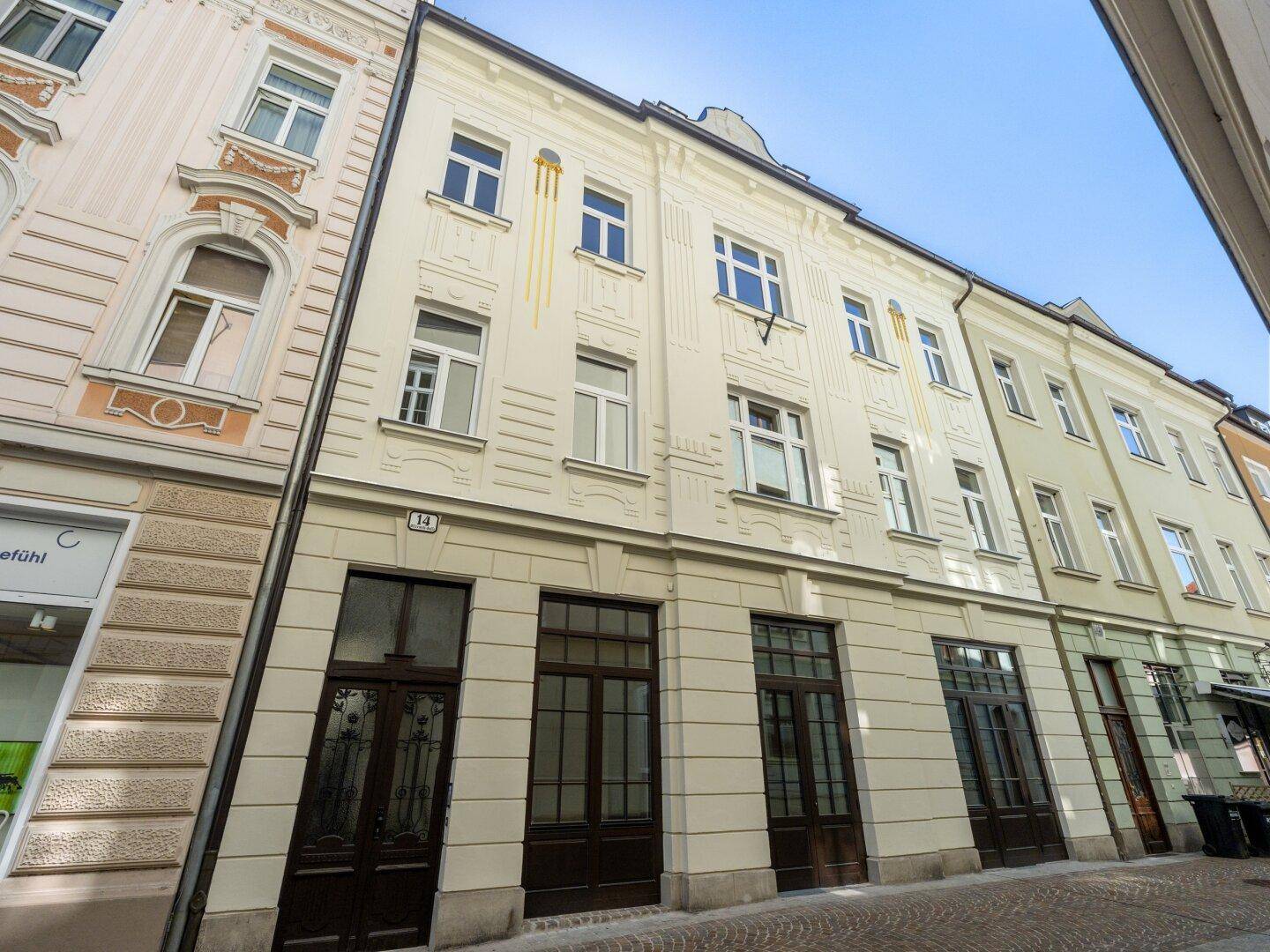 Historische Fassade eines Stadthauses mit mehreren Fenstern und Geschäften im Erdgeschoss.