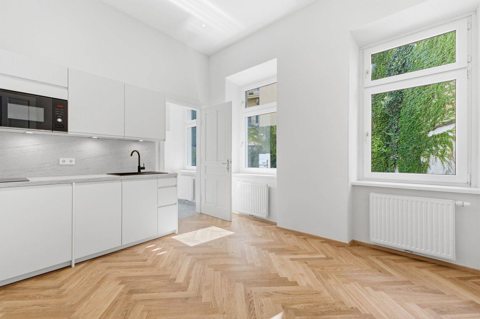 Moderne weiße Küche mit integrierten Geräten, Fischgrätparkett und einem schönen Blick ins Grüne.