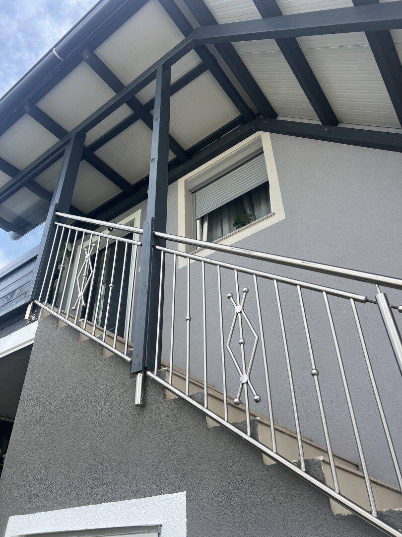 Außenansicht eines Hauses mit Treppe und modernem Edelstahlgeländer unter einem Vordach.