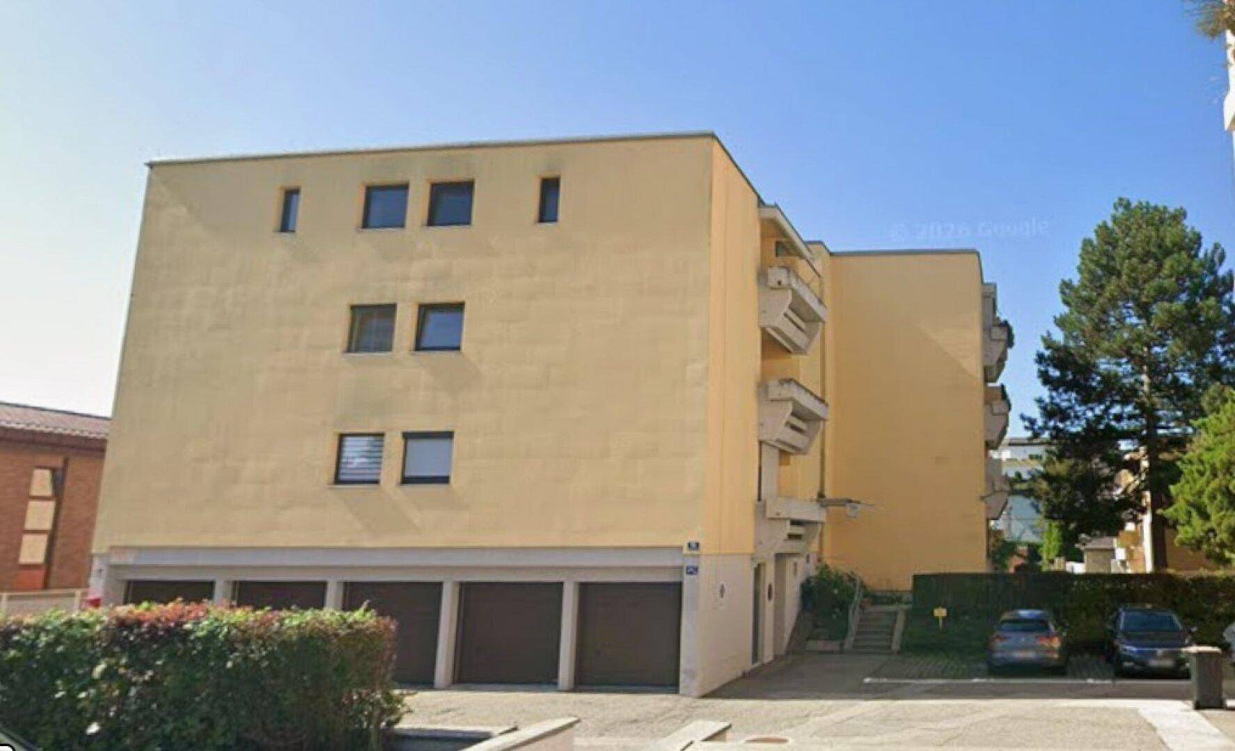 Gelbes Mehrfamilienhaus mit mehreren Fenstern, Balkonen und Garagen im Erdgeschoss.