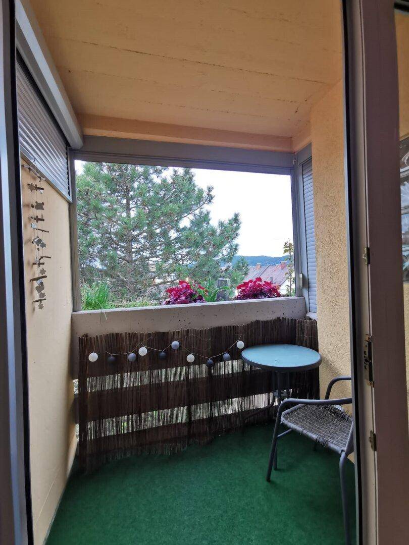 Gemütlicher Balkon mit Kunstrasen, kleinem Tisch und Stuhl, bietet einen grünen Ausblick.