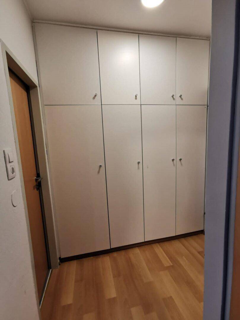 Flur mit praktischen, hellgrauen Einbauschränken und einem warmen Holzfußboden.