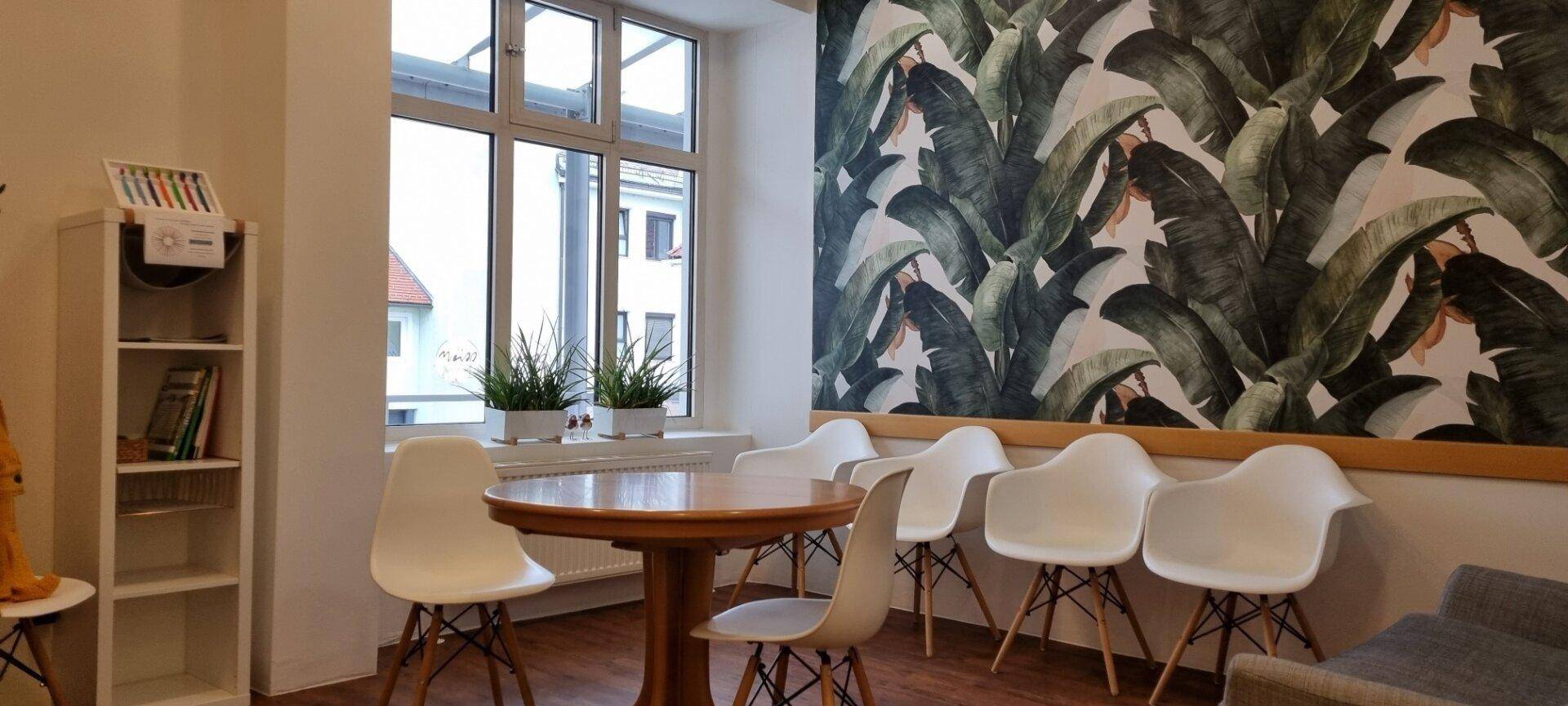 Helles Wartezimmer mit tropischer Tapete, Holztisch und modernen weißen Stühlen, einladend gestaltet.