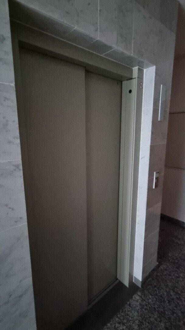 Geschlossene Aufzugtür aus Metall in einem gefliesten Flur, bereit zur Benutzung und gut gepflegt.