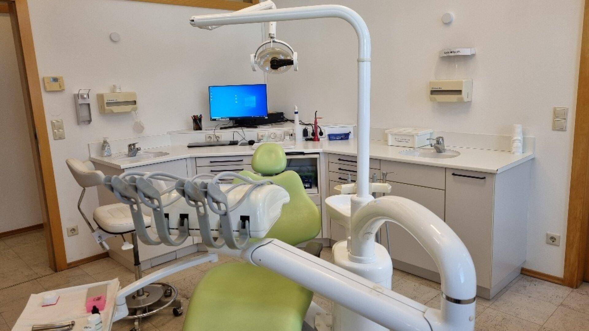 Modernes Behandlungszimmer mit zahnmedizinischem Stuhl, Computermonitor und weißen Schränken, effizient eingerichtet.