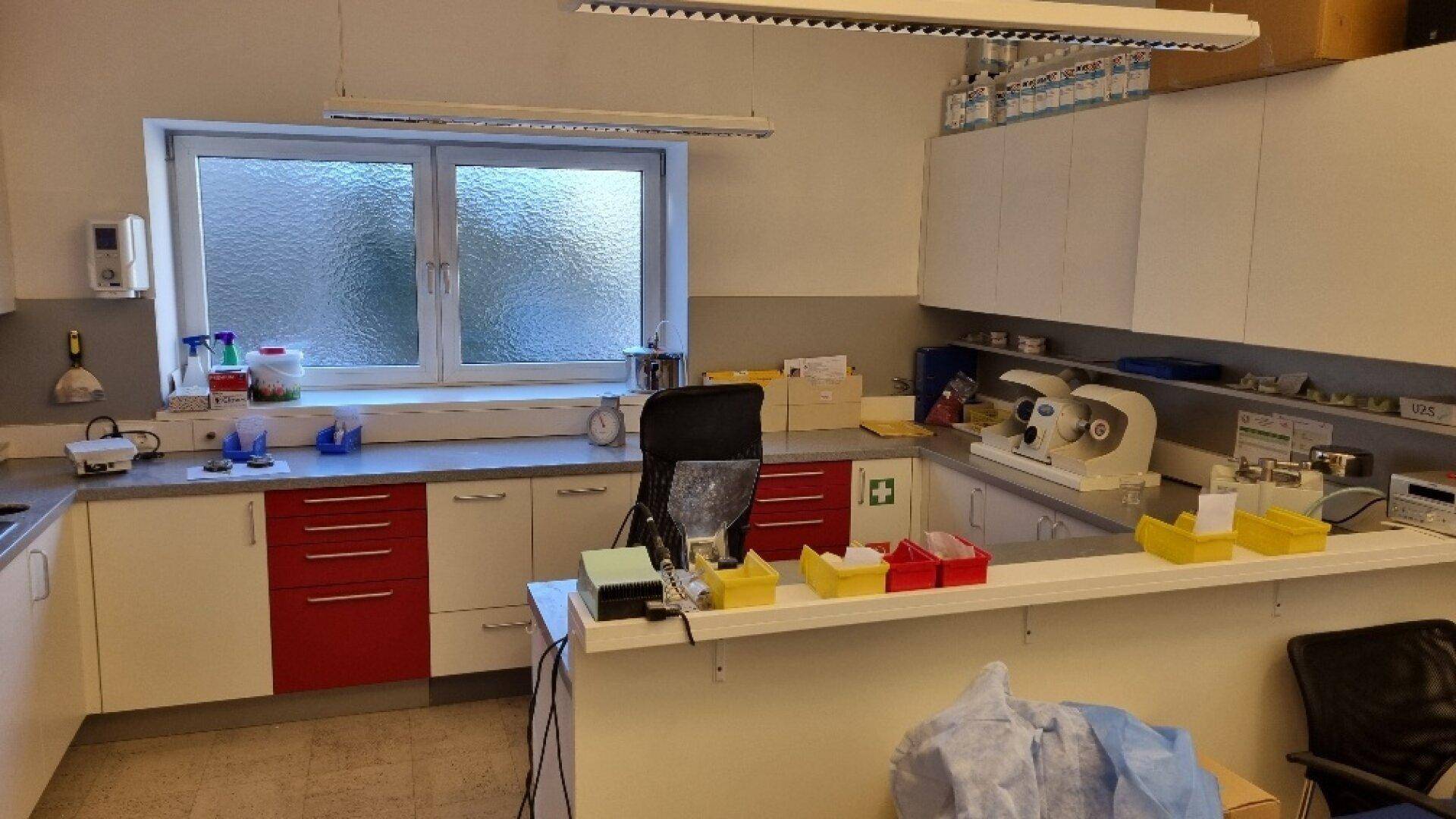 Zahntechnisches Labor mit Arbeitsflächen, roten und weißen Schränken und Spezialgeräten, gut organisiert.