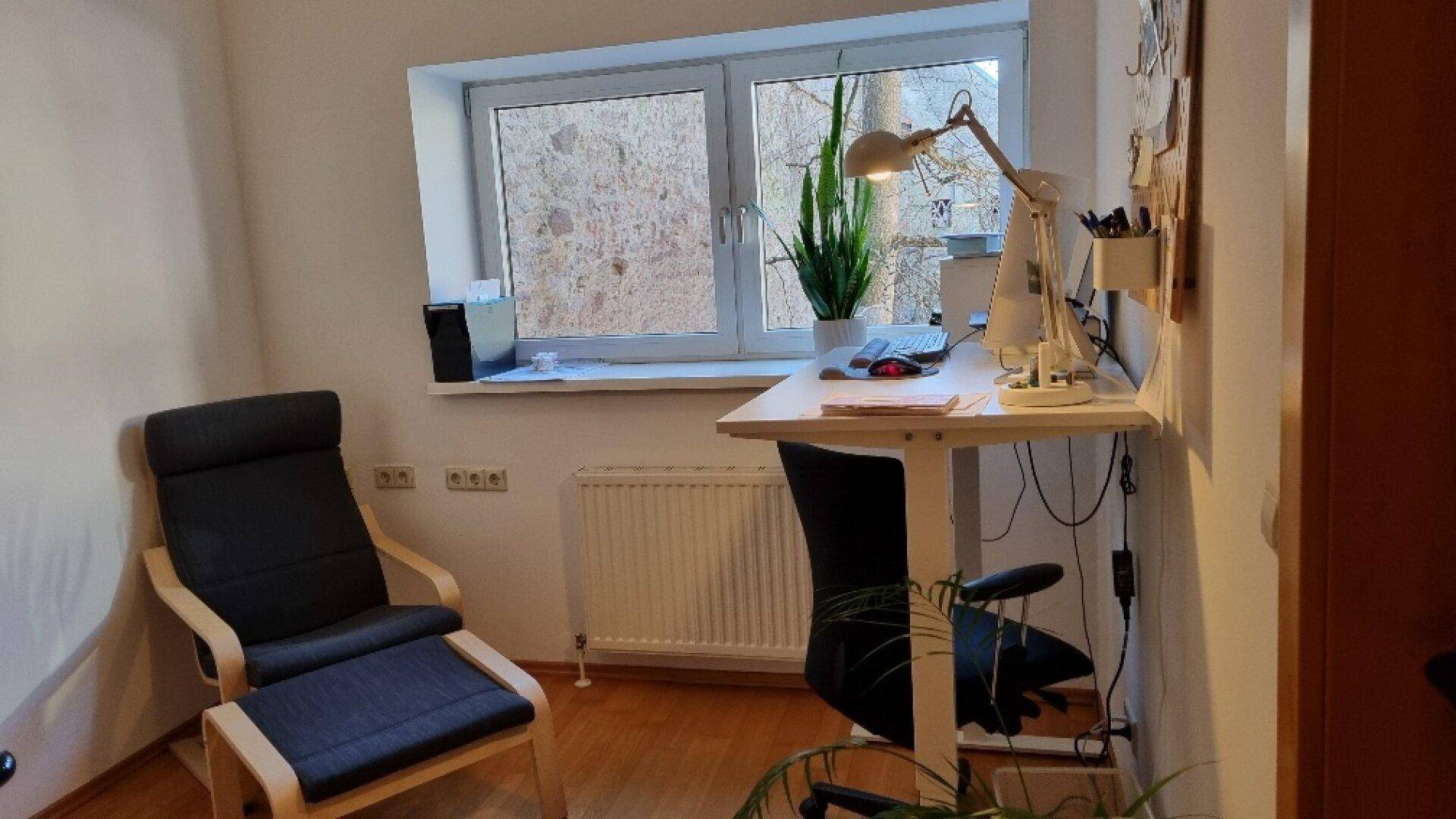 Helles Büro mit Schreibtisch, Bürostuhl, Sessel und Fenster mit Blick ins Grüne, ideal zum Arbeiten.