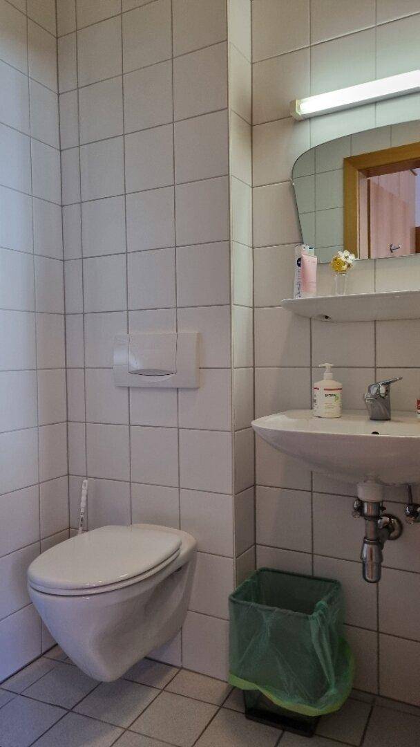 Toilette mit wandhängendem WC, Waschbecken und weißen Fliesen, einfach und funktional eingerichtet.