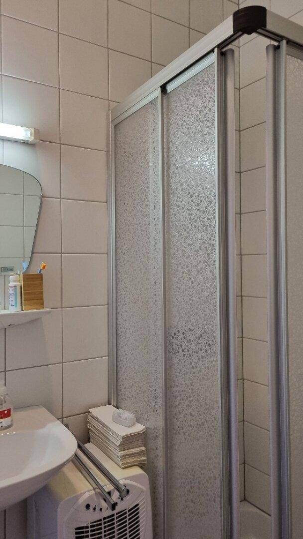 Badezimmer mit Duschkabine, Waschbecken und weißen Fliesen, sauber und gepflegt für den täglichen Gebrauch.