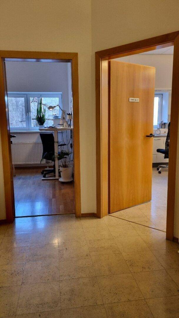 Flur mit Holztüren, Fliesenboden und Blick in angrenzende Büroräume, hell und einladend.
