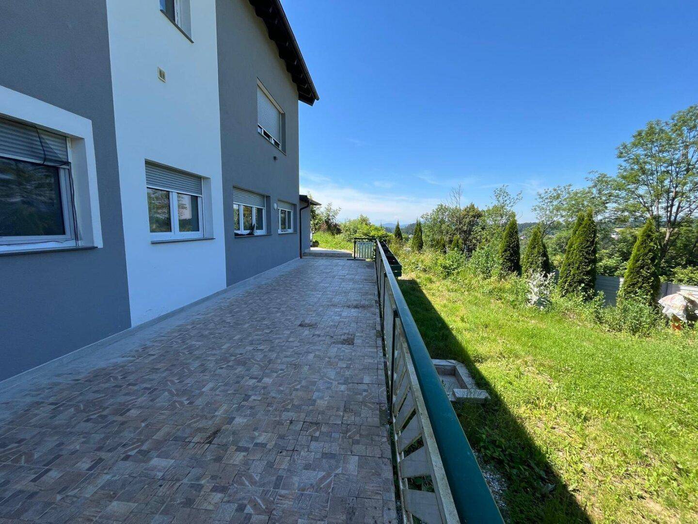 Lange geflieste Terrasse entlang des Hauses mit Blick ins Grüne und auf die umliegende Landschaft.