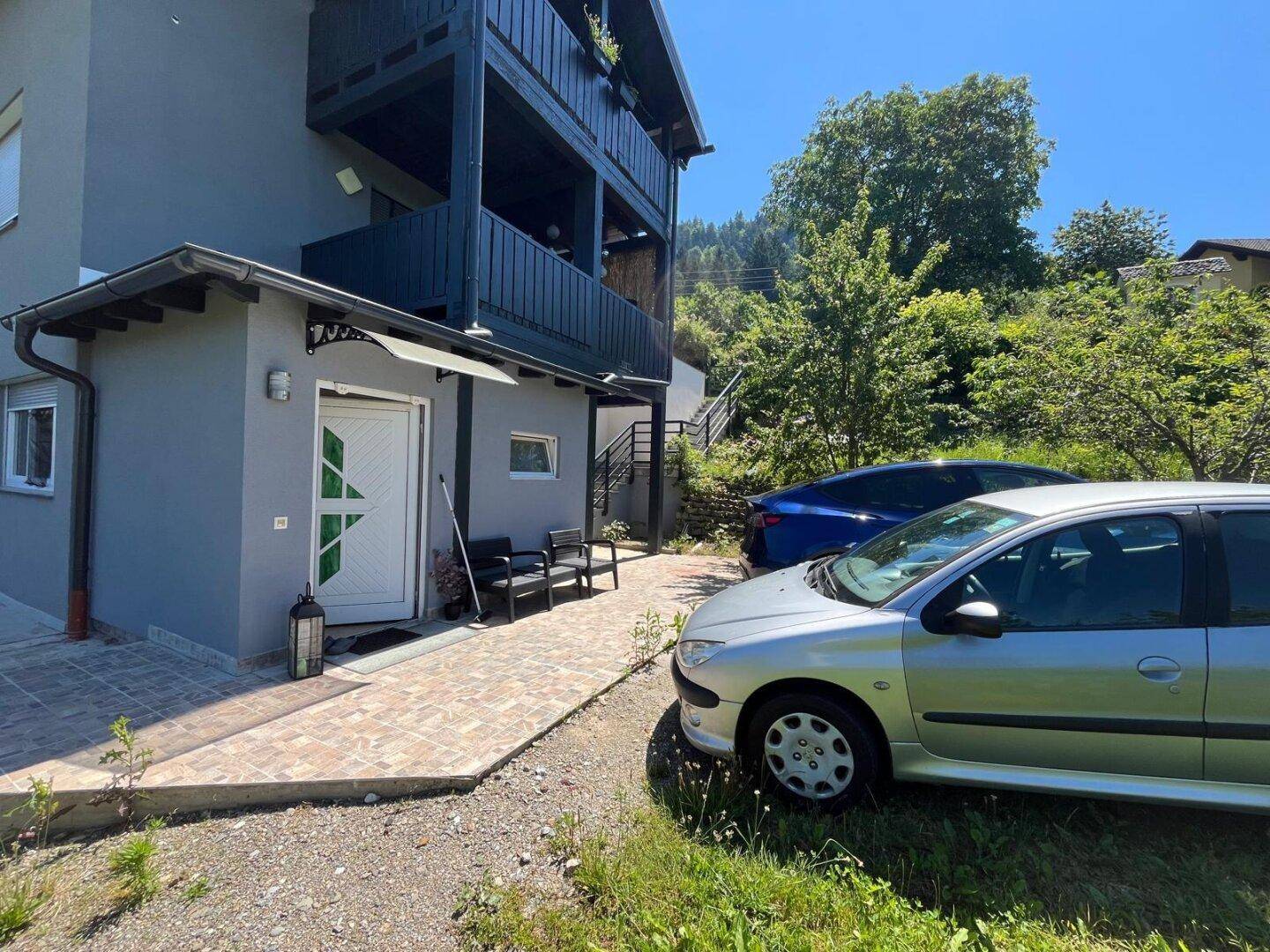 Außenansicht des Hauses mit Eingangsbereich und zwei geparkten Fahrzeugen auf dem Vorplatz.