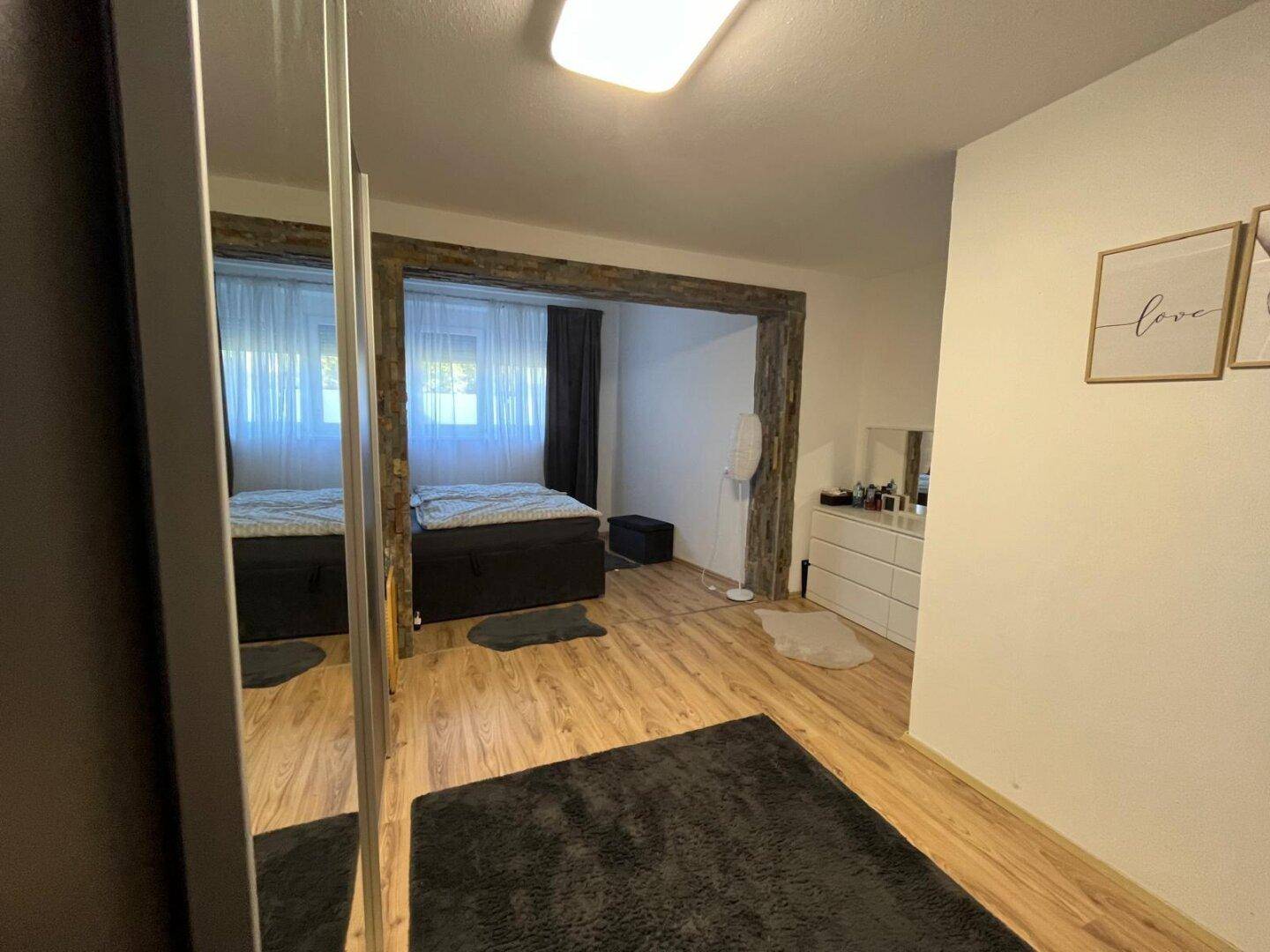 Helles Schlafzimmer mit großem Spiegelschrank und Holzfußboden, der den Raum optisch vergrößert.
