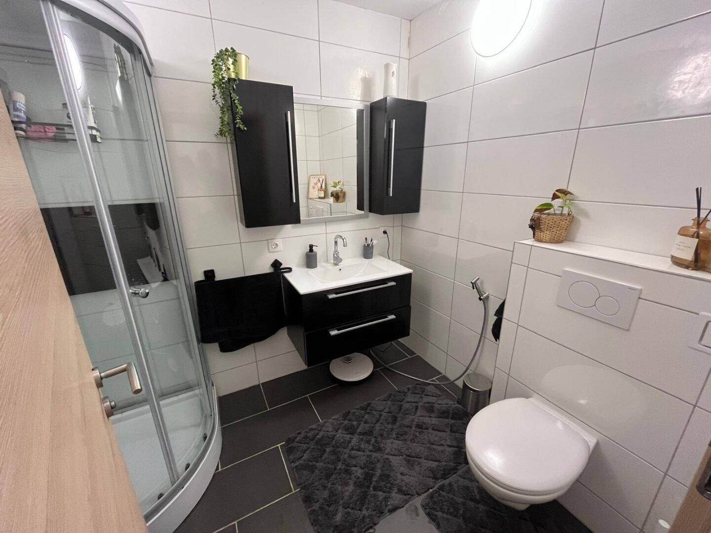 Modernes Badezimmer mit Duschkabine, WC und Waschtisch, ausgestattet mit weißen und grauen Fliesen.