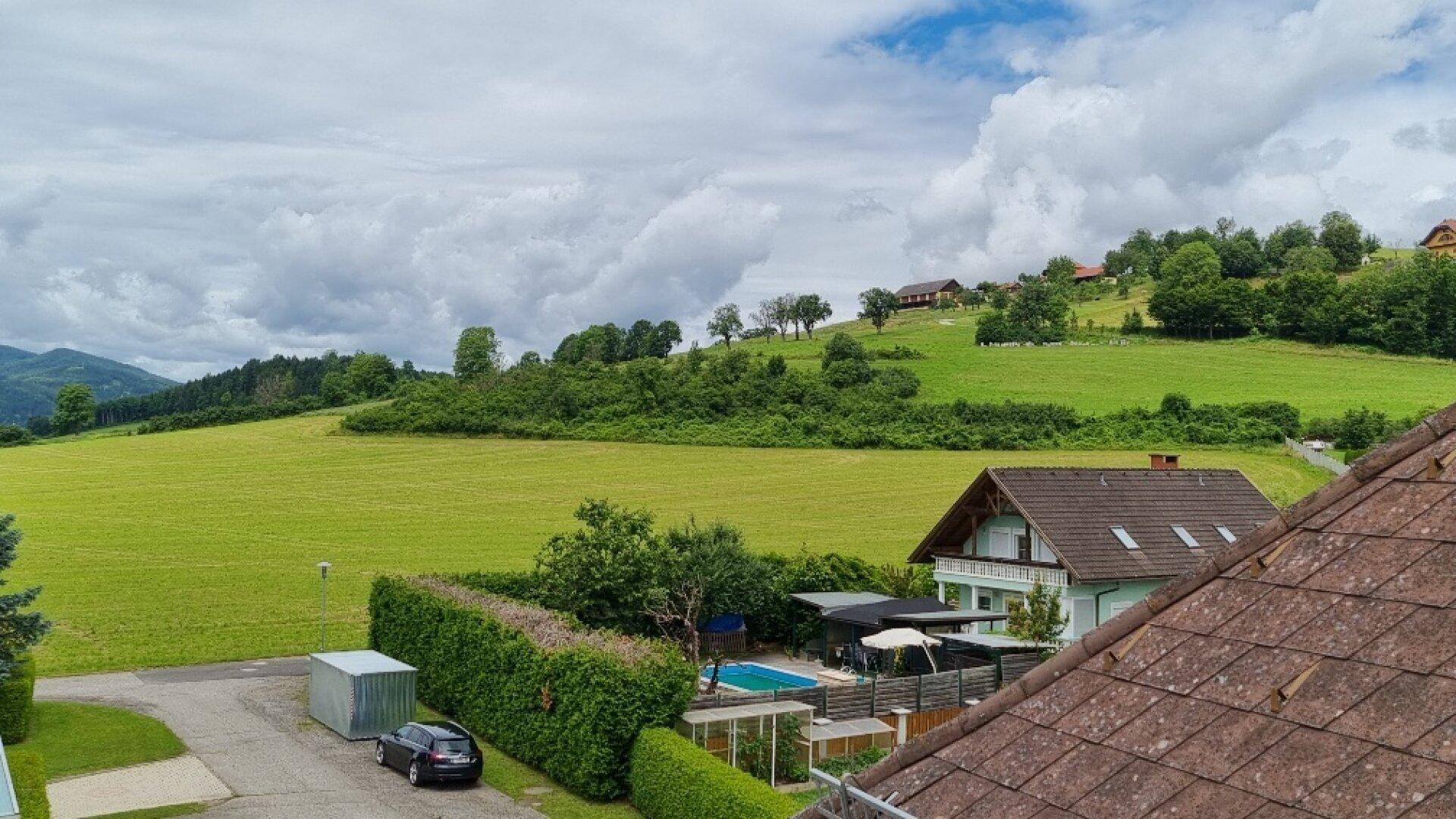 Panoramablick über grüne Felder und Hügel mit einem Haus und einem Pool im Vordergrund.