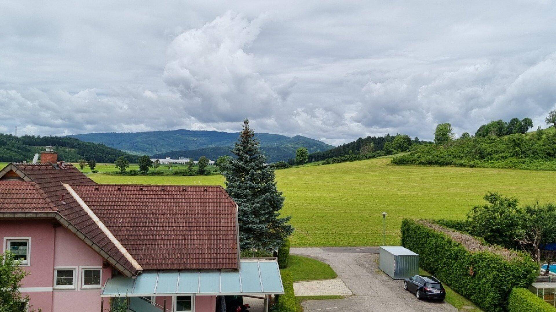 Blick auf die umliegende grüne Landschaft mit Hügeln und einem Teil eines rosa Hauses.