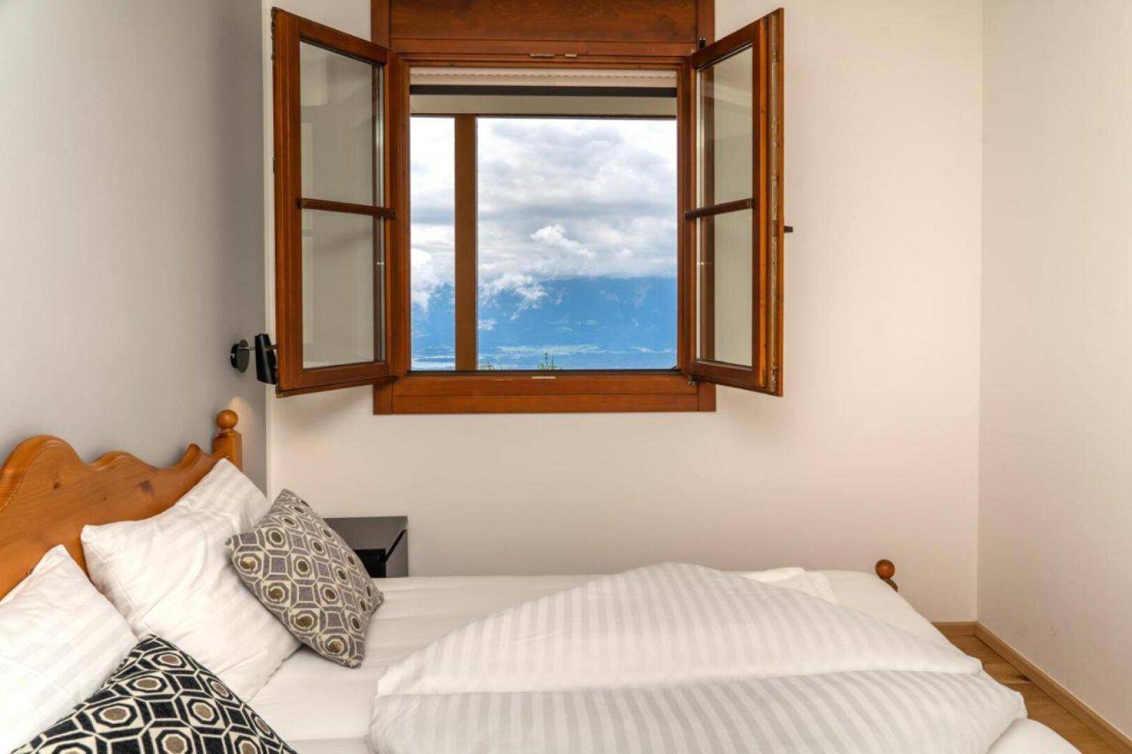 Helles Schlafzimmer mit Holzbett und Fenster, das einen weiten Blick auf die Berge bietet.