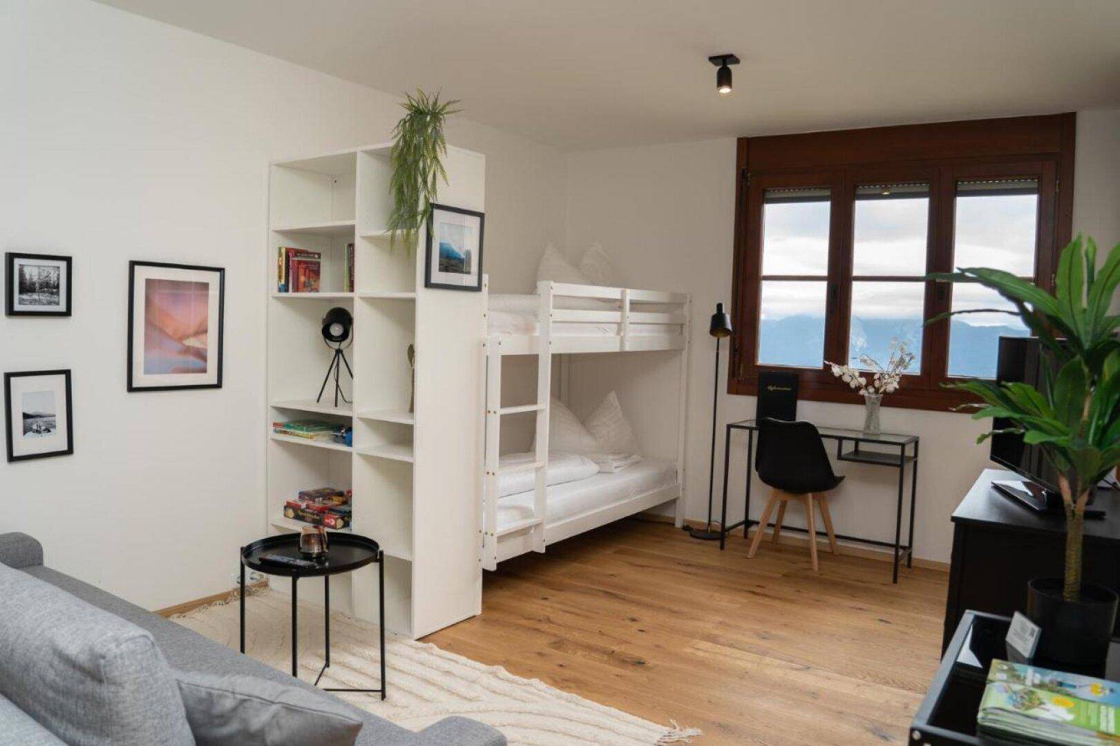 Heller Wohnbereich mit Etagenbett, Schreibtisch und Regal, ideal für Familien oder Gäste.