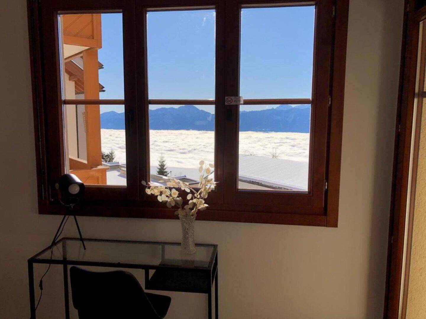 Fenster mit weitem Blick auf eine schneebedeckte Berglandschaft und Wolkenmeer.