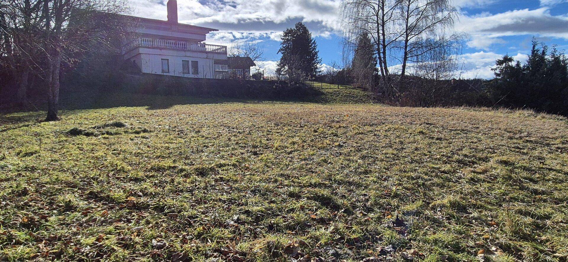 Große Wiesenfläche mit einem traditionellen Haus im Hintergrund unter bewölktem Himmel.