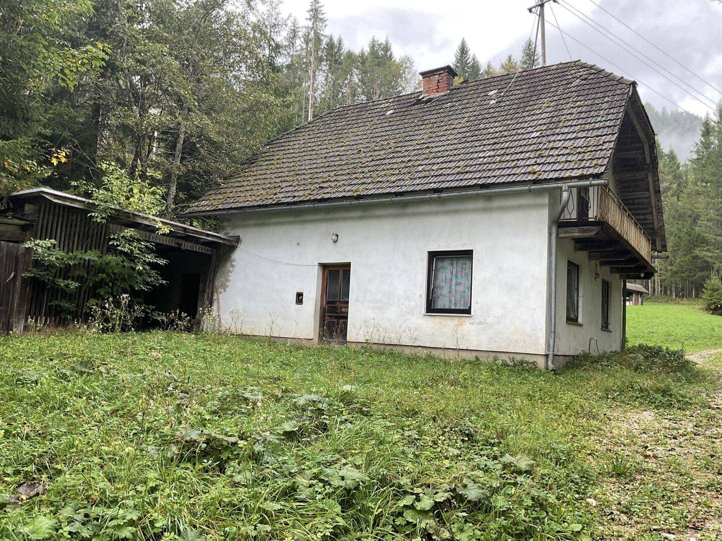 Vorderansicht des Bauernhauses mit Holztür und kleinem Balkon, umgeben von üppigem Grün.