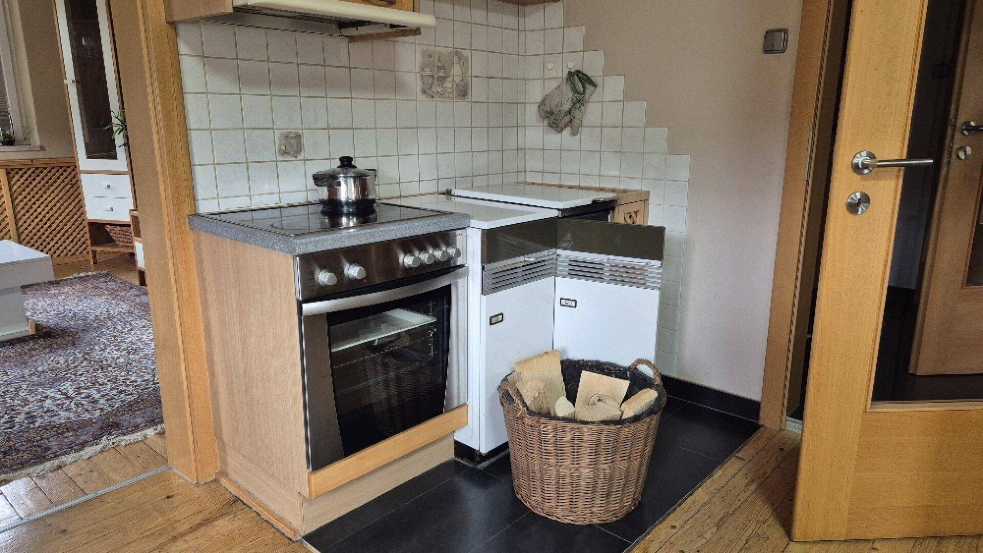 Kleine, funktionale Küche mit Herd, Backofen und Holzkorb, ideal für den täglichen Gebrauch.