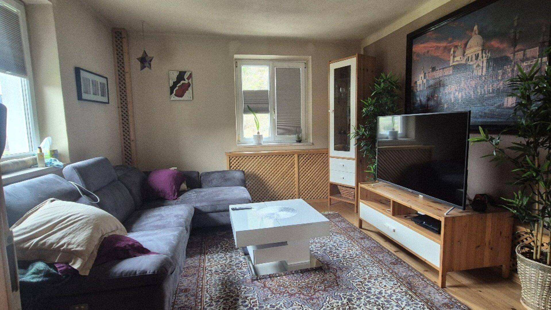 Gemütliches Wohnzimmer mit großem Ecksofa, Teppich und Fernseher, ideal zum Entspannen.