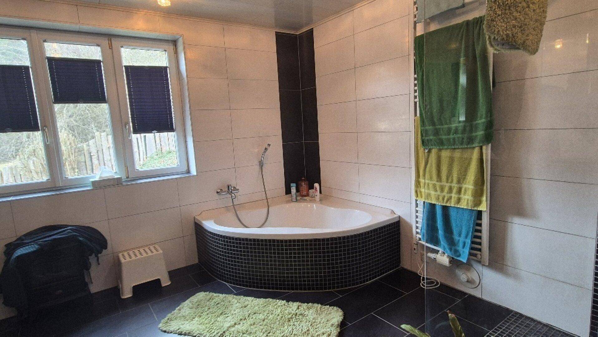 Badezimmer mit Eckbadewanne, Fenster und beheiztem Handtuchhalter, in Schwarz-Weiß-Fliesen.