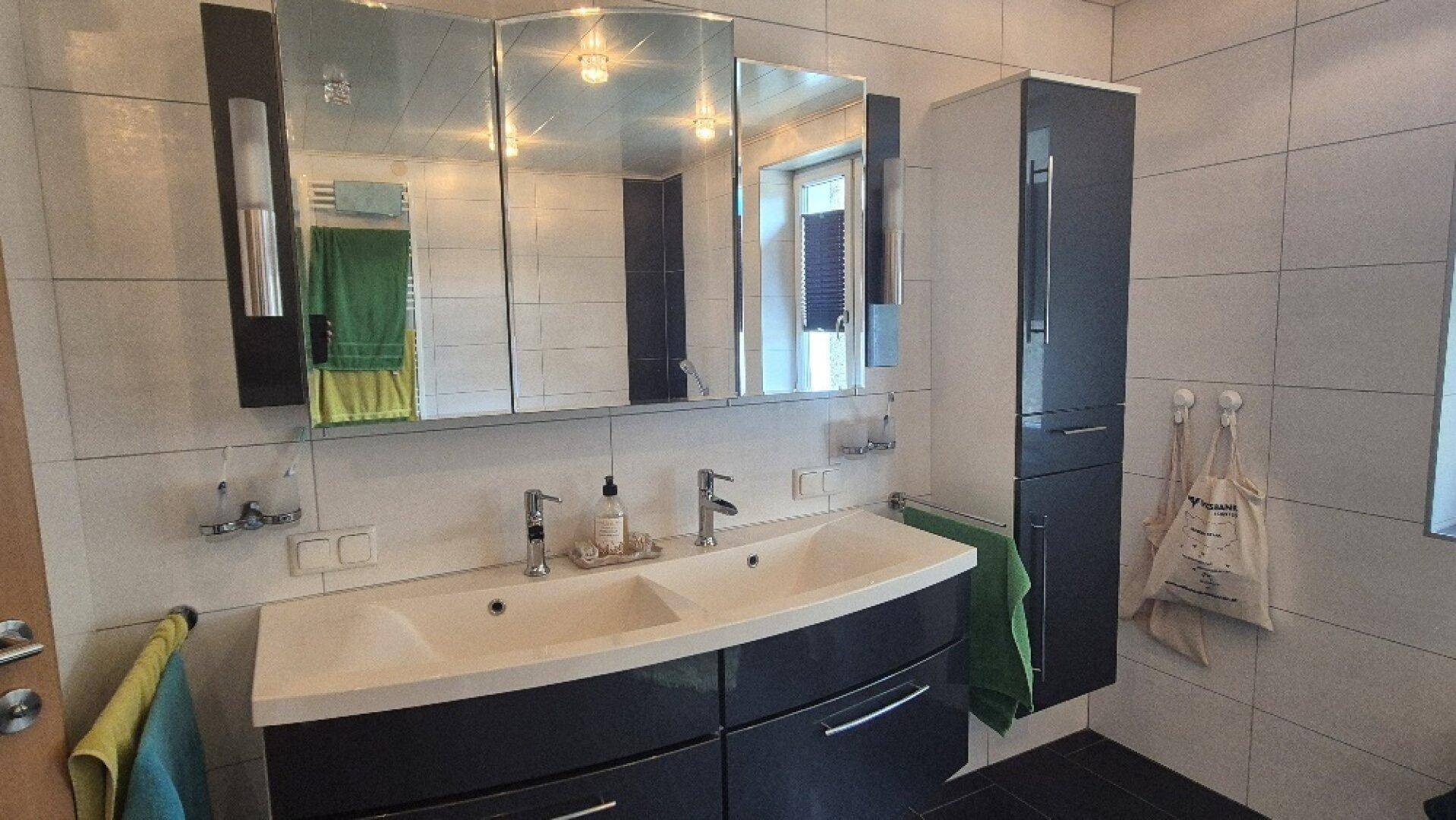 Badezimmer mit Doppelwaschbecken, Spiegelschrank und modernen dunklen Badmöbeln.