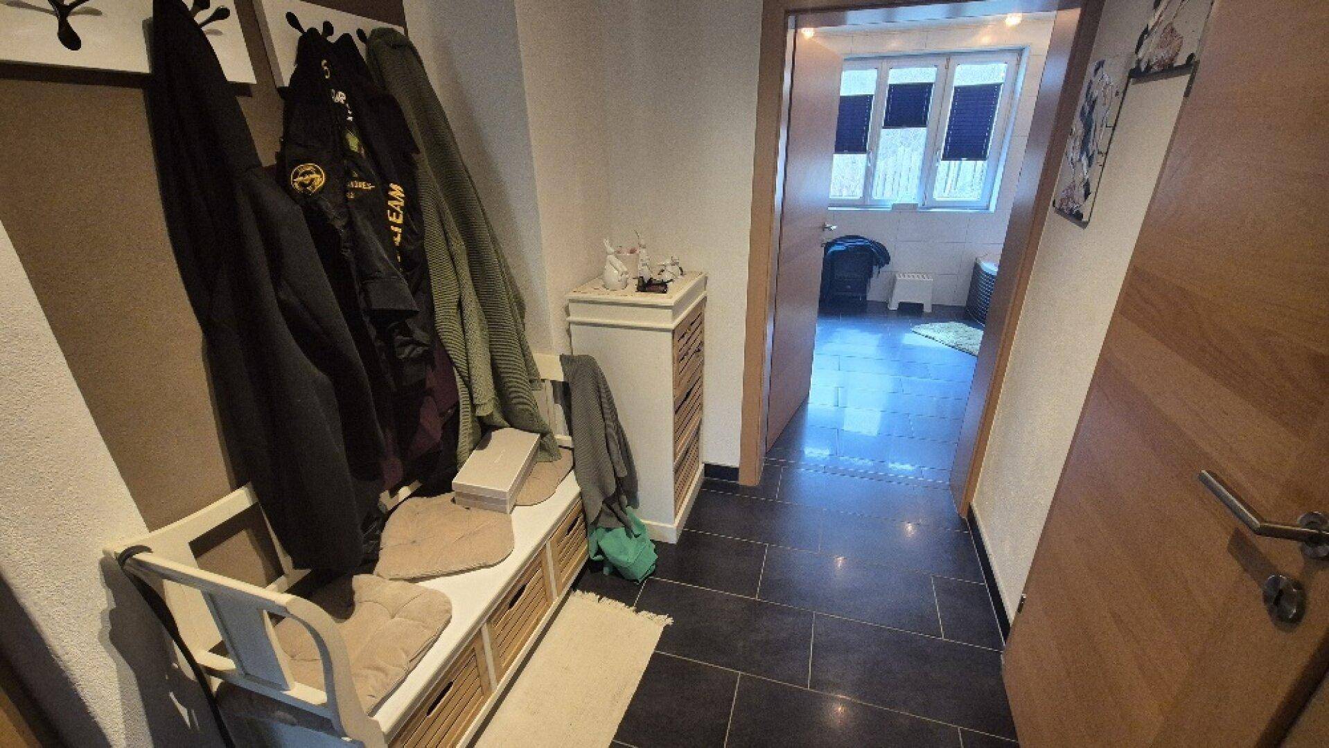 Eingangsbereich mit Garderobe, Sitzbank und dunklen Fliesen, führt zu weiteren Räumen.